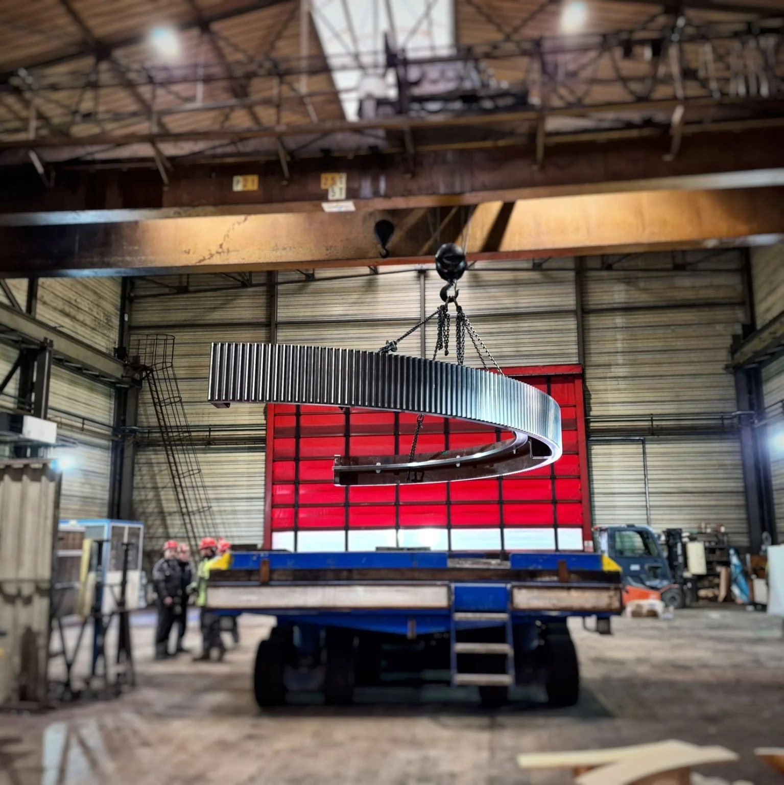 Half segment of a large girth gear lifted by overhead crane in a fabrication shop